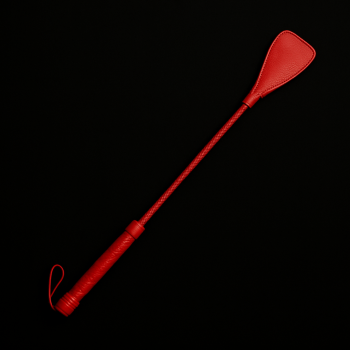 Fusta de cuero rojo sobre fondo negro, herramienta simbólica utilizada en prácticas de spanking y juegos de disciplina BDSM